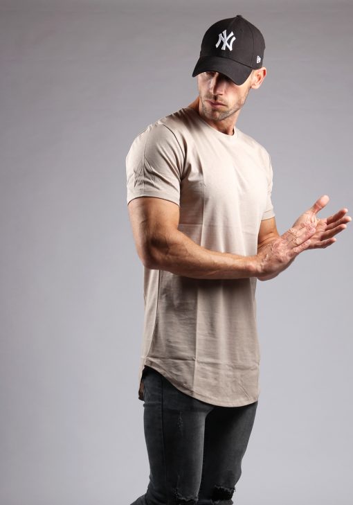 Rechter vooraanzicht heren T-shirt in desert kleur en een slimfit pasvorm. Het model draagt een donkere jeans, een zwarte pet en wrijft in zijn handen.