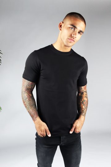 Vooraanzicht heren T-shirt in zwarte kleur en een straight fit pasvorm. Het model draagt een donkere jeans en heeft zijn beide handen in zijn broekzakken.
