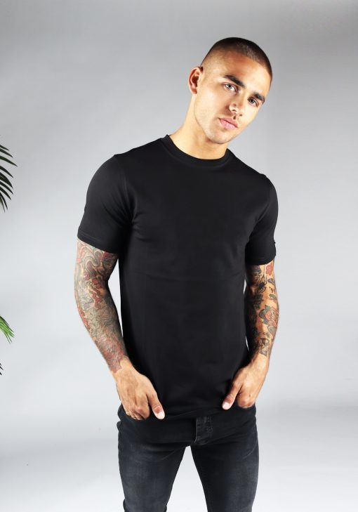Vooraanzicht heren T-shirt in zwarte kleur en een straight fit pasvorm. Het model draagt een donkere jeans en heeft zijn beide handen in zijn broekzakken.