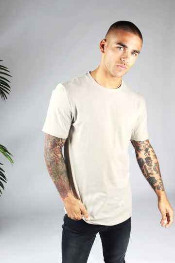 Vooraanzicht heren T-shirt in sand kleur en een long fit pasvorm. Het model draagt een donkere jeans en heeft zijn rechterhand in zijn rechter broekzak.