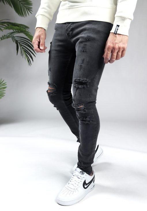 Linker zijaanzicht zwarte damaged heren skinny jeans met broekzakken, knoopsluiting en riemlussen. Gecombineerd met witte sweater en witte sneakers.