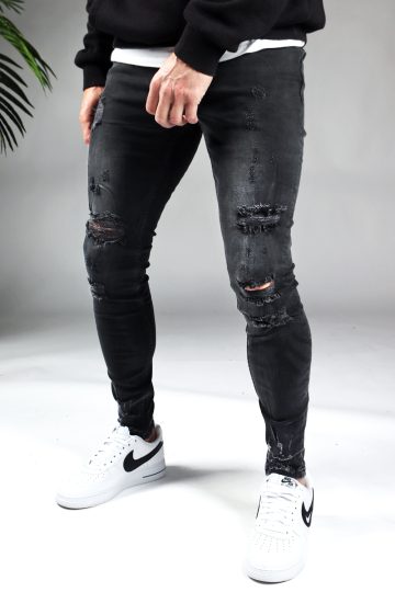 Voorkant zwarte damaged heren skinny jeans met broekzakken, knoopsluiting en riemlussen. Gecombineerd met zwarte sweater en witte sneakers.