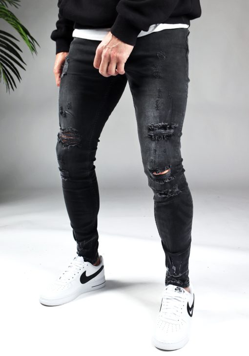 Voorkant zwarte damaged heren skinny jeans met broekzakken, knoopsluiting en riemlussen. Gecombineerd met zwarte sweater en witte sneakers.