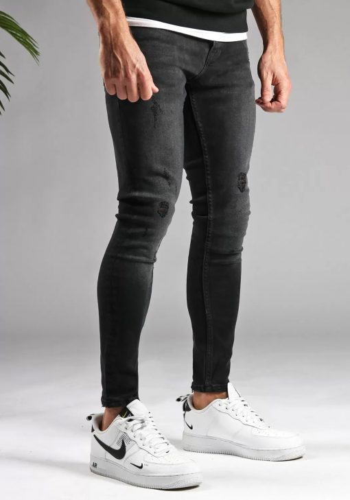Rechter zijaanzicht zwarte denmin heren jeans skinny pasvorm, damaged uitstraling, broekzakken en knoopsluiting. Gecombineerd met zwarte hoodie en witte sneakers.