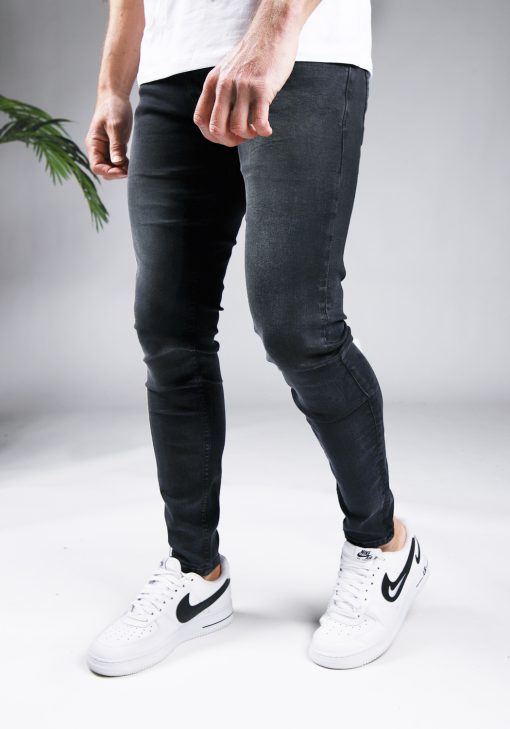 Linker zijaanzicht zwarte heren skinny jeans met twee broekzakken, twee kontzakken en knoopsluiting. Gecombineerd met witte sneakers en een wit T-shirt.