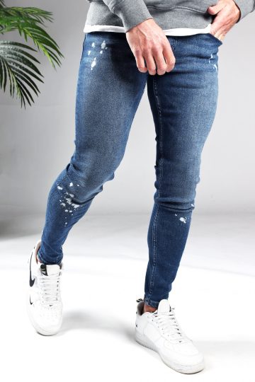 Voorkant denim heren jeans skinny fit met damaged look, broekzakken, knoopsluiting en riemlussen. Gecombineerd met grijze hoodie en witte sneakers.