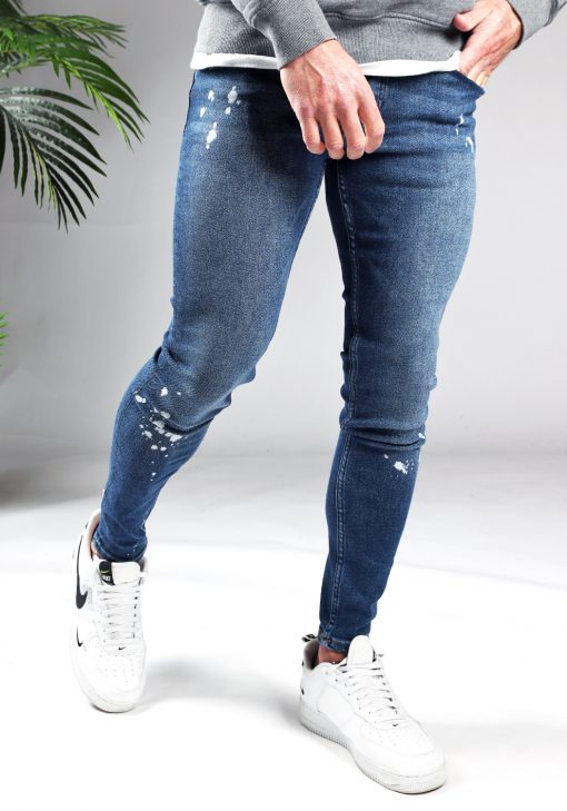 Voorkant denim heren jeans skinny fit met damaged look, broekzakken, knoopsluiting en riemlussen. Gecombineerd met grijze hoodie en witte sneakers.