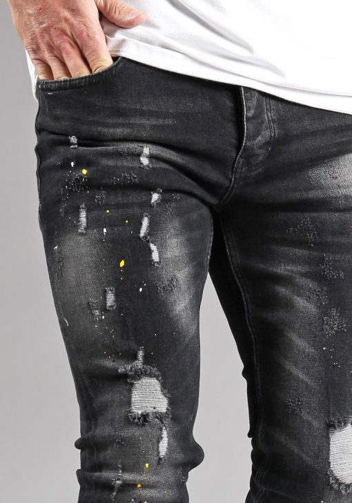Close up broekspijp bovenbeen donkergrijze damaged heren skinny jeans met gele en witte verfspetters.