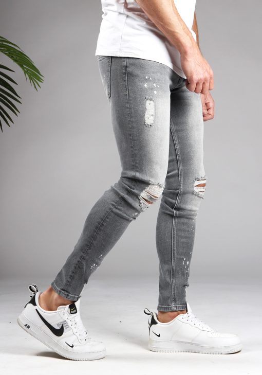 Rechter zijkant lichtgrijze denim heren skinny jeans met damaged look, scheuren en verfspatten. Gecombineerd met wit T-shirt en witte sneakers.