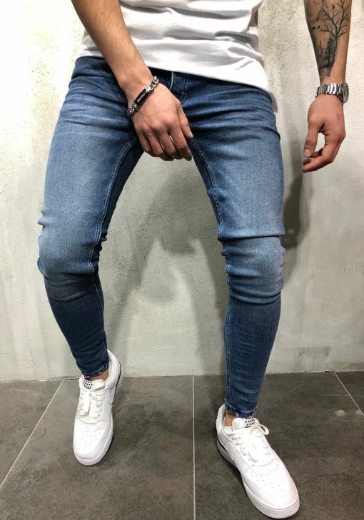 Vooraanzicht blauwe heren jeans skinny pasvorm met twee broekzakken, twee kontzakken, knoopsluiting en riemlussen. Gecombineerd met wit T-shirt en witte sneakers.
