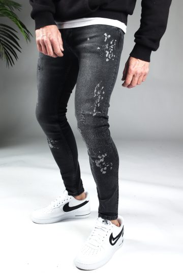 Linker zijaanzicht donkergrijze denim heren skinny jeans met lichte verfspetters. Gecombineerd met zwarte hoodie en witte sneakers.