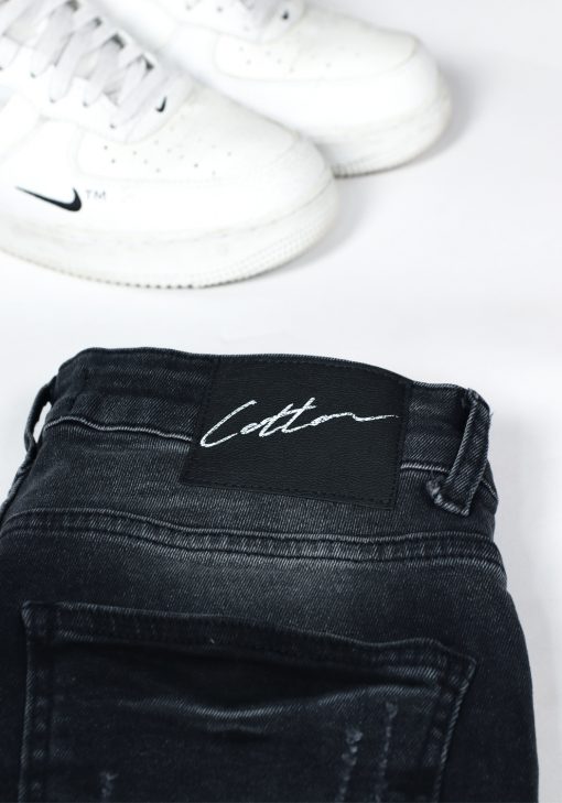 Close up Cotton-logo op achterkant donkergrijze denim heren skinny jeans met lichte verfspetters.
