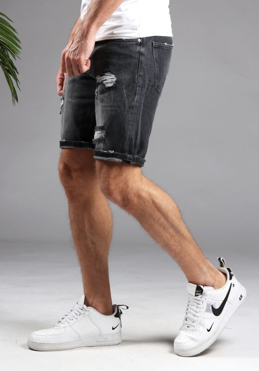 Zijaanzicht van model gekleed in donkergrijze shorts met damaged details. Het model heeft zijn armen langs zich en draagt een wit shirt.