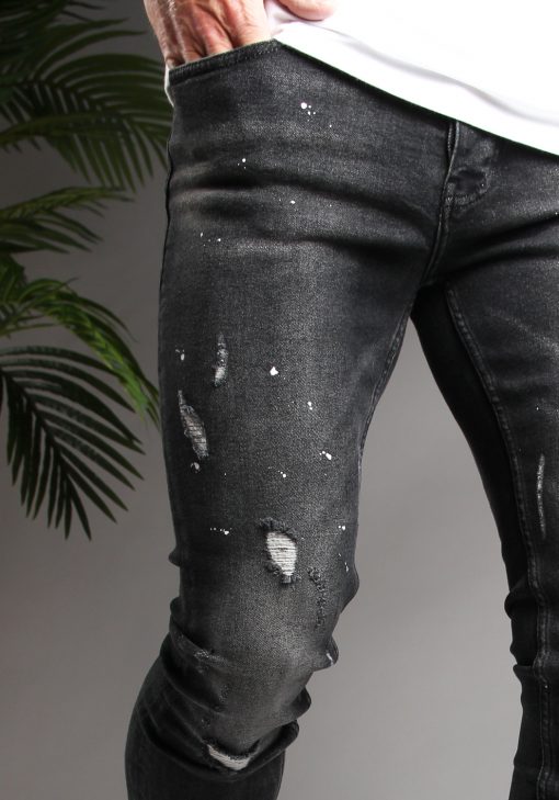 Close up broekzak en bovenbeen zwarte heren skinny jeans met verfspetters en kleine scheuren, gemaakt van stretch stof.