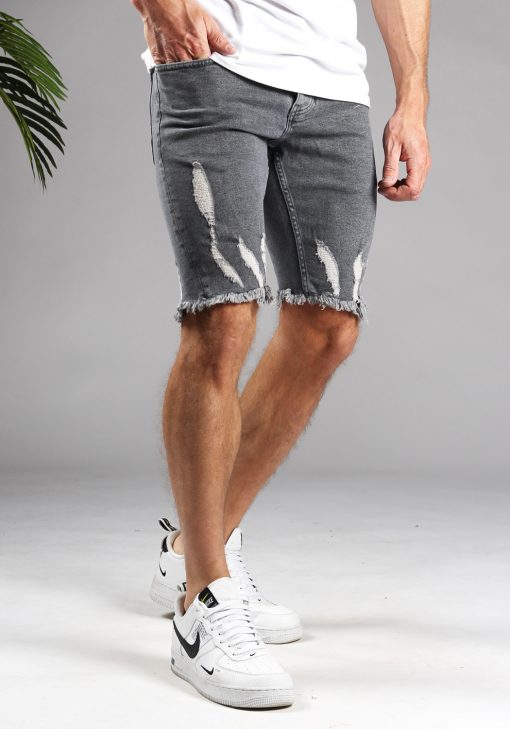 Schuin vooraanzicht van model gekleed in grijze shorts met damaged details. Het model heeft een hand in zijn zak en draagt een wit shirt.
