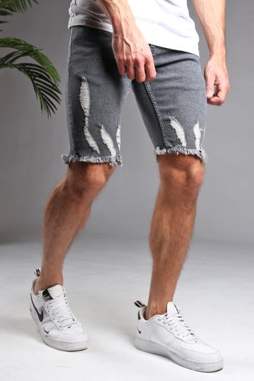 Schuin vooraanzicht van model gekleed in grijze shorts met damaged details. Het model heeft zijn handen langs zijn lichaam en draagt een wit shirt.