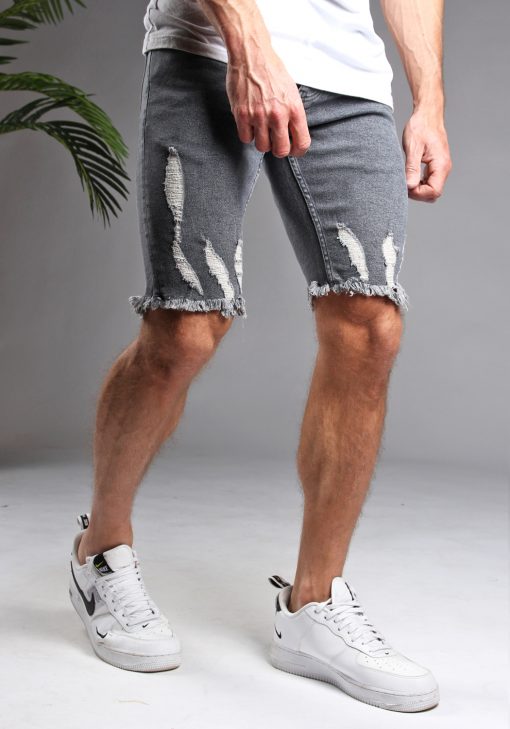 Schuin vooraanzicht van model gekleed in grijze shorts met damaged details. Het model heeft zijn handen langs zijn lichaam en draagt een wit shirt.