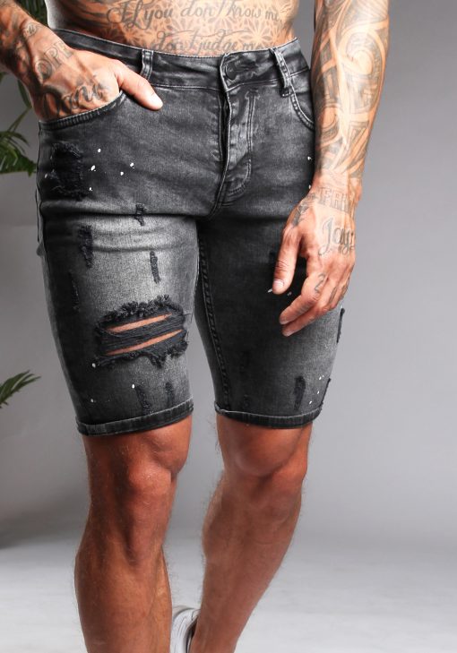 Vooraanzicht van model gekleed in grijze jean shorts met damaged details en verfspetters. Het model heeft een hand in zijn broekzak.