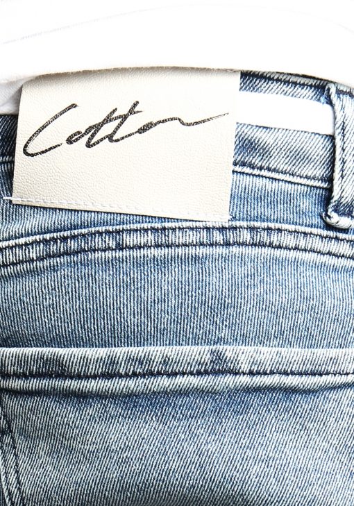 Close up van wit label aan de achterkant van de lichtblauwe jean shorts met daarop het zwarte signature Cotton District logo.