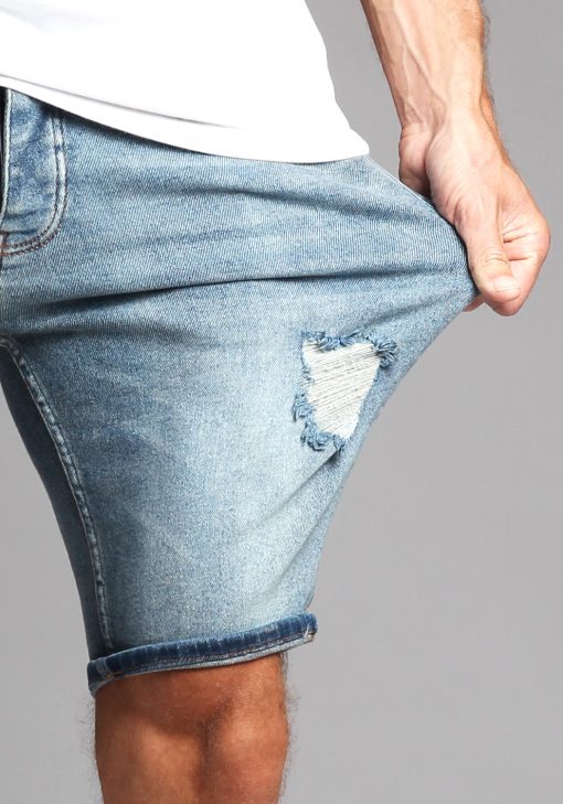 Close up van lichtblauwe jean shorts waarbij het model aan de broek trekt en hierdoor de stretch zichtbaar is.