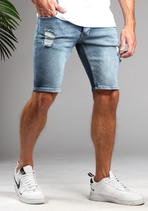 Linker vooraanzicht van model gekleed in lichtblauwe jean shorts met damaged details Het model heeft een hand in de broekzak en staat met een been naar achteren.