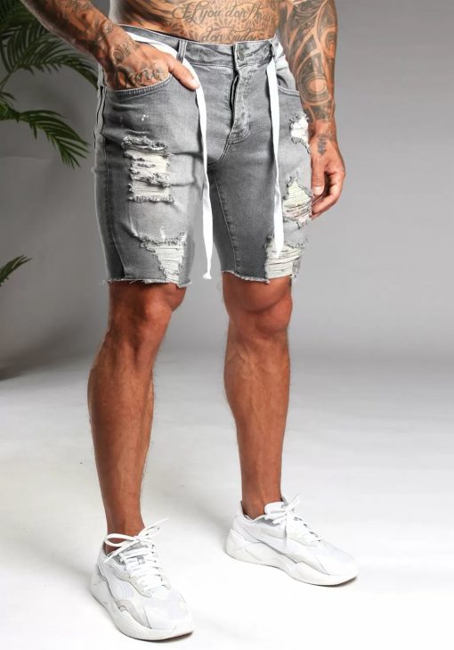 Schuin rechter vooraanzicht van model gekleed in grijze jean shorts. De shorts hebben damaged details en een wit touw door de riemgaten. Het model heeft een hand in zijn zak.