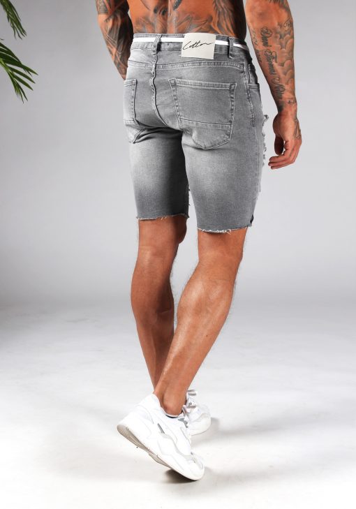 Achteraanzicht van model gekleed in grijze jean shorts in combinatie met witte sneakers. De shorts hebben damaged details en een wit touw door de riemgaten.