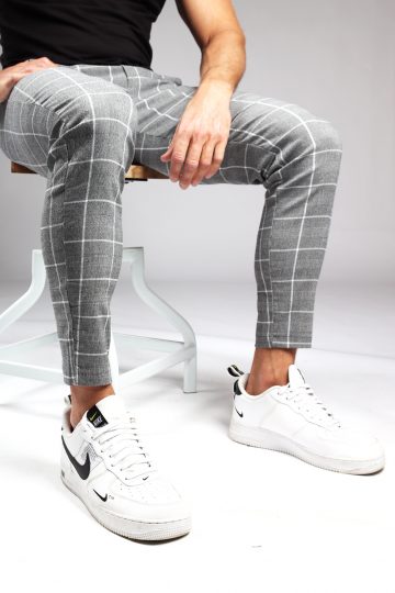 Model met heren chino grijs met witte ruit, gemaakt van stretch stof en met skinny pasvorm zit op een kruk. Chino broek is met broekzakken en knoopsluiting.