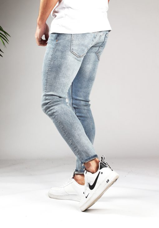 Zijaanzicht lichtblauwe heren jeans met skinny fit, twee zakken aan de voorzijde, twee achterzakken, knoopsluiting en riemlussen. Gecombineerd met witte sneakers en een wit T-shirt.