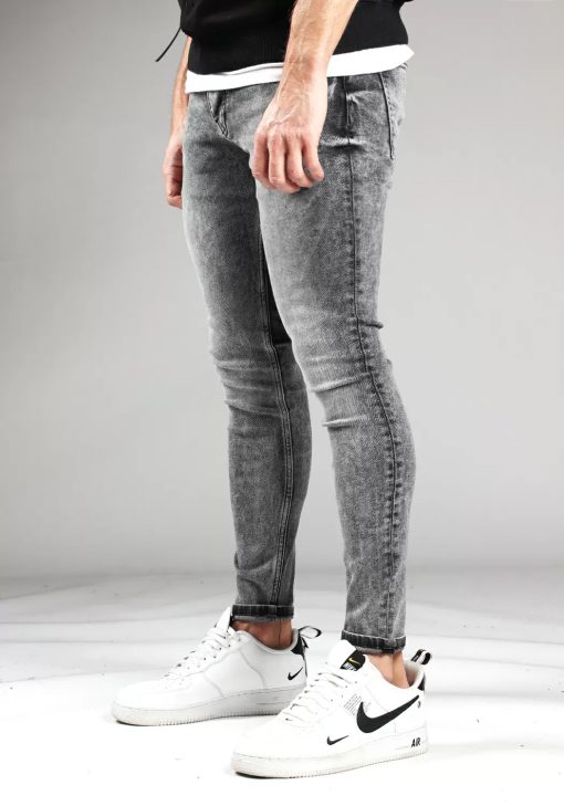 Linker zijkant grijze heren skinny jeans met broekzakken, knoopsluiting en riemlussen. Gecombineerd met zwarte hoodie en witte sneakers.
