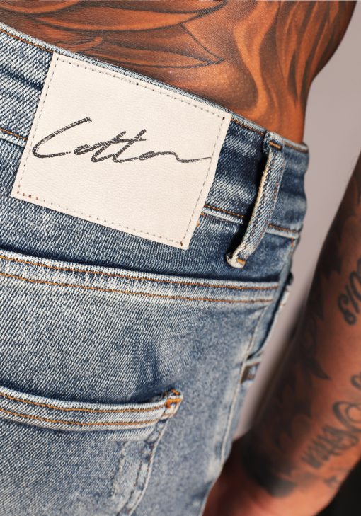 Close up Cotton-logo op achterkant lichtblauwe damaged heren skinny jeans met broekzakken, knoopsluiting en riemlussen.