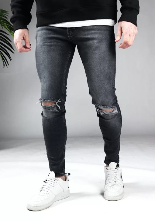 Voorkant donkergrijze heren skinny jeans met scheuren bij de knieën, gemaakt van stretch stof. Voorzien van vier zakken, knoopsluiting en riemlussen. Gecombineerd met zwarte sweater en witte sneakers.