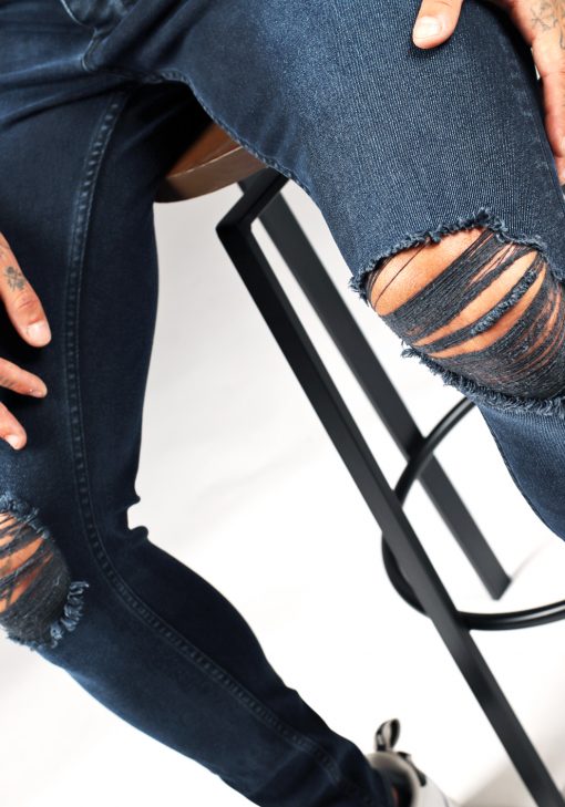 Close up scheur bij knie op donkerblauwe denim heren skinny jeans met damaged look, scheuren en verfspatten.