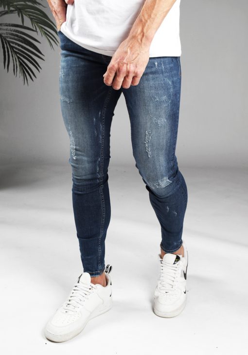 Linker zijaanzicht denim heren skinny jeans met damaged look, gemaakt van stretch stof. Voorzien van vier zakken, knoopsluiting en riemlussen. Gecombineerd met wit T-shirt en witte sneakers.