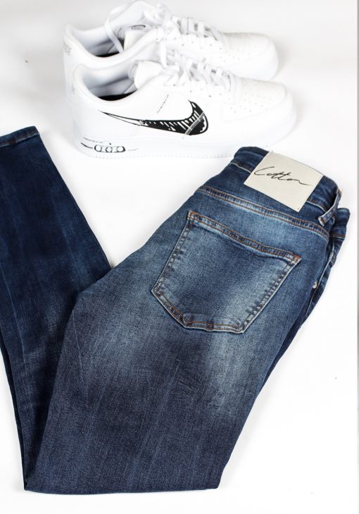 Close up achterkant blauwe denim heren skinny jeans met verwassen look en Cotton-logo. Voorzien van twee broekzakken, twee kontzakken, knoopsluiting en riemlussen.
