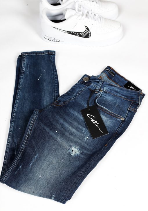 Voorzijde opgevouwen blauwe damaged denim heren skinny jeans met verfspetters.