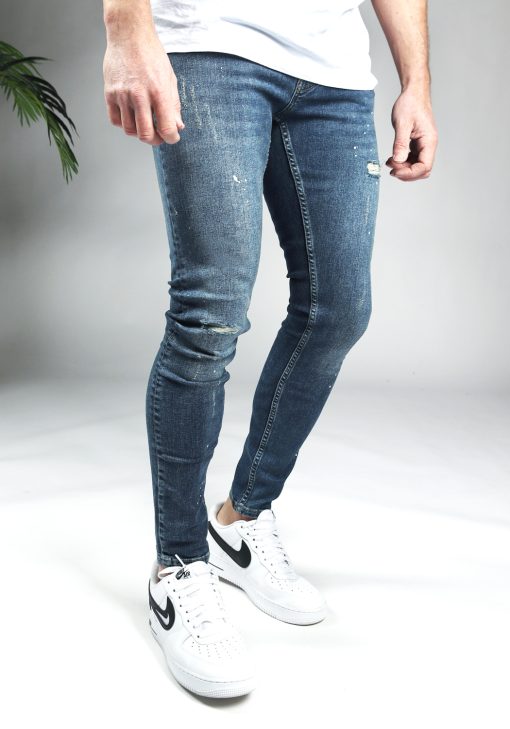 Rechter zijkant blauwe damaged denim heren skinny jeans met verfspetters.