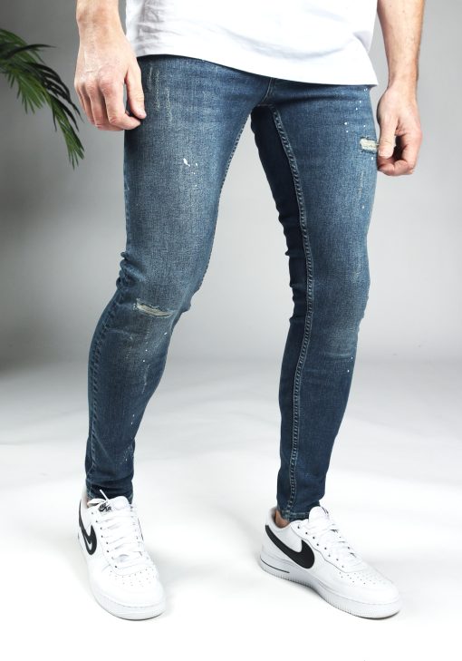 Rechter zijkant blauwe damaged denim heren skinny jeans met verfspetters.