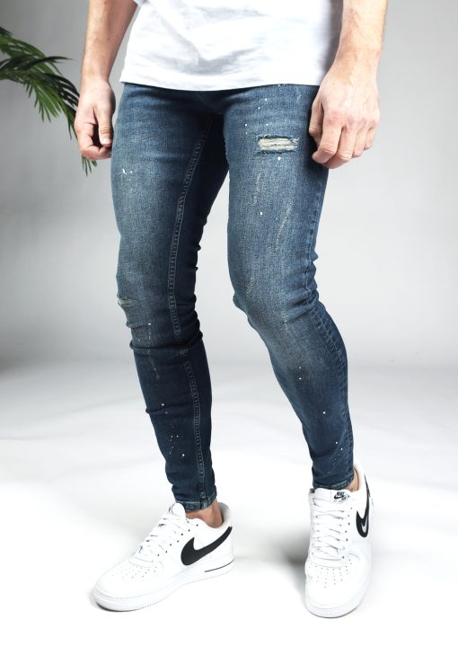 Linker zijkant blauwe damaged denim heren skinny jeans met verfspetters.