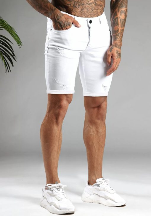Rechter vooraanzicht van model gekleed in witte jean shorts met damaged details in combinatie met witte sneakers. Het model heeft een hand in zijn broekzak.