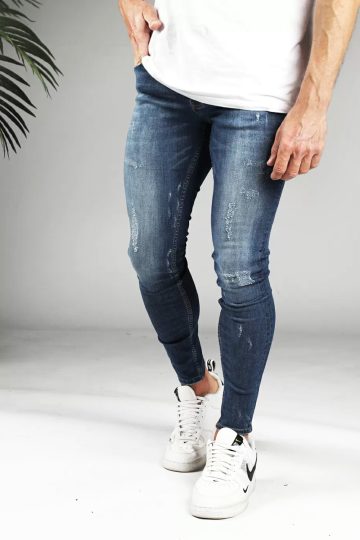 Voorkant denim heren skinny jeans met damaged look, gemaakt van stretch stof. Voorzien van vier zakken, knoopsluiting en riemlussen. Gecombineerd met wit T-shirt en witte sneakers.