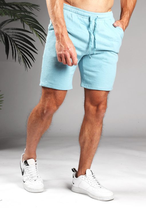 Vooraanzicht van model gekleed in lichtblauwe jog shorts met touwtjes. Het model heeft een hand in zijn zak en draagt witte sneakers.