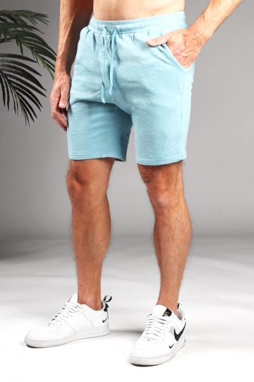 Schuin vooraanzicht van model gekleed in lichtblauwe jog shorts met touwtjes. Het model heeft een hand in zijn zak en draagt witte sneakers.
