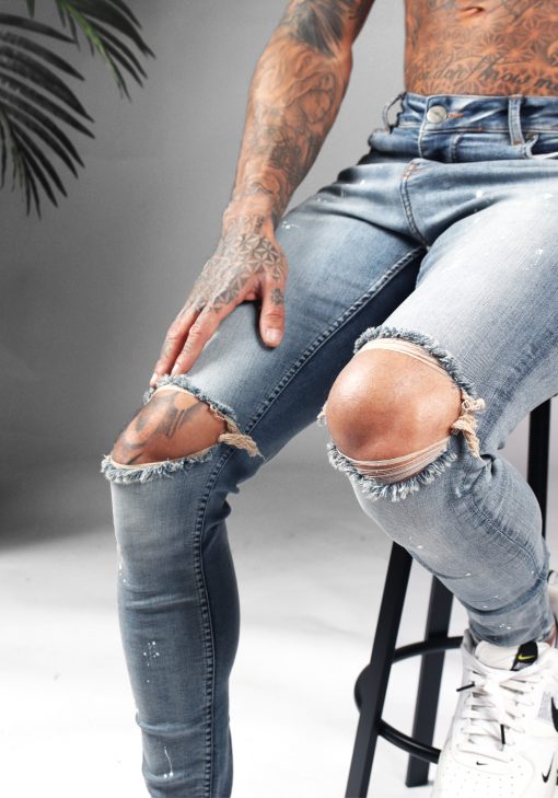 Close up gescheurde knieën van blauwe denim heren jeans met skinny pasvorm, gescheurde knieën en verfspetters.