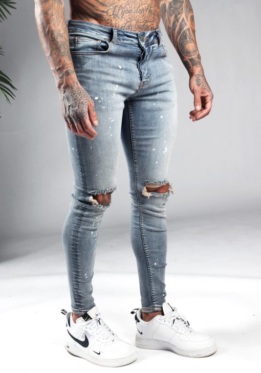 Rechter zijkant blauwe denim heren jeans met skinny pasvorm, gescheurde knieën en verfspetters.