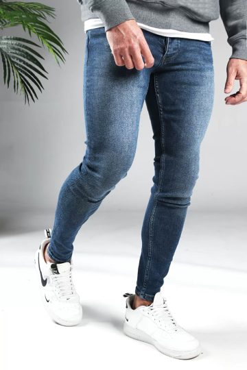 Rechter zijaanzicht blauwe heren jeans skinny pasvorm met twee broekzakken, twee kontzakken, knoopsluiting en riemlussen. Gecombineerd met grijze sweater en witte sneakers.