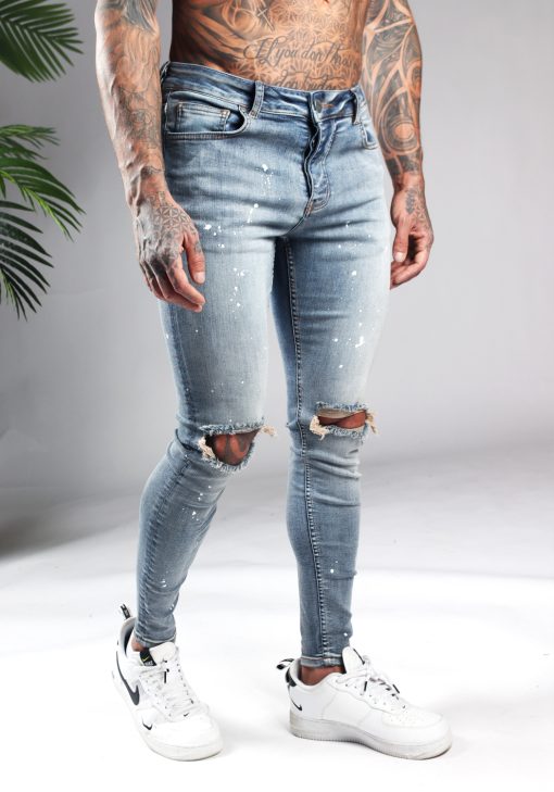 Rechter zijkant blauwe denim heren jeans met skinny pasvorm, gescheurde knieën en verfspetters.