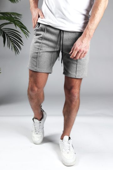 Vooraanzicht comfortabele heren chino shorts in grijze kleur, met skinny fit en gemaakt van luxe stretch stof. Voorzien van twee broekzakken en rekbare taille met trekkoord. Gecombineerd met witte sneakers en een wit T-shirt.