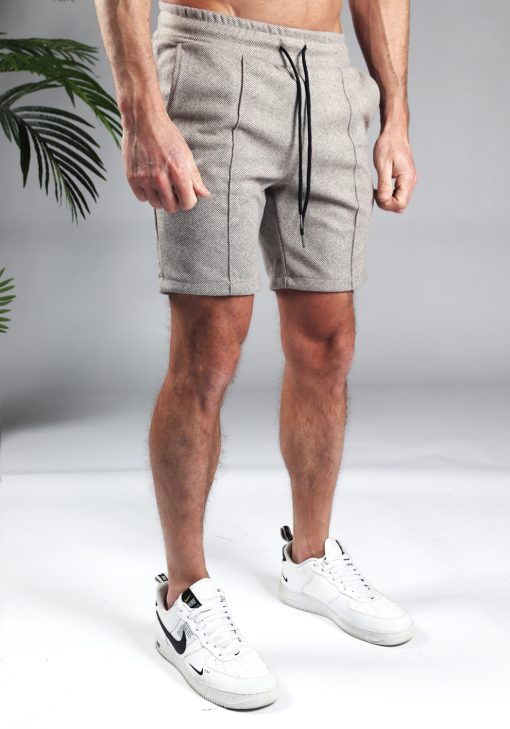 Vooraanzicht comfortabele heren chino shorts in zandkleur, met skinny fit en gemaakt van luxe stretch stof. Voorzien van twee broekzakken en rekbare taille met zwart trekkoord. Gecombineerd met witte sneakers.