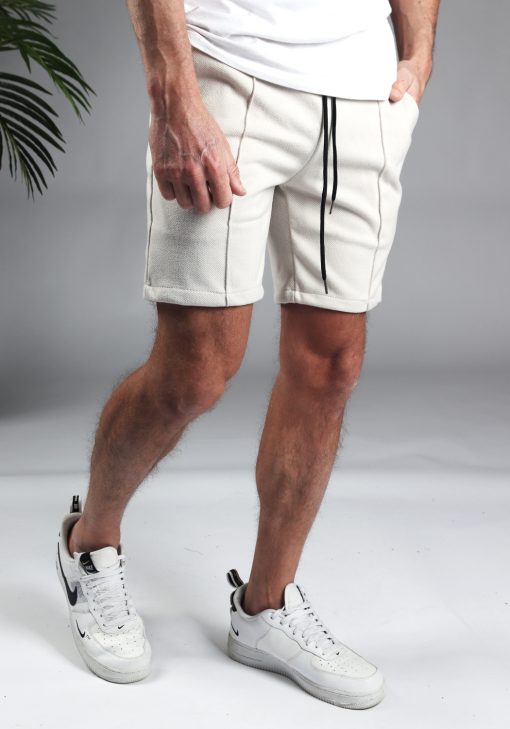 Rechter zijaanzicht comfortabele heren chino shorts in off white, met skinny fit en gemaakt van luxe stretch stof. Voorzien van twee broekzakken en rekbare taille met zwart trekkoord. Gecombineerd met witte sneakers en een wit T-shirt.